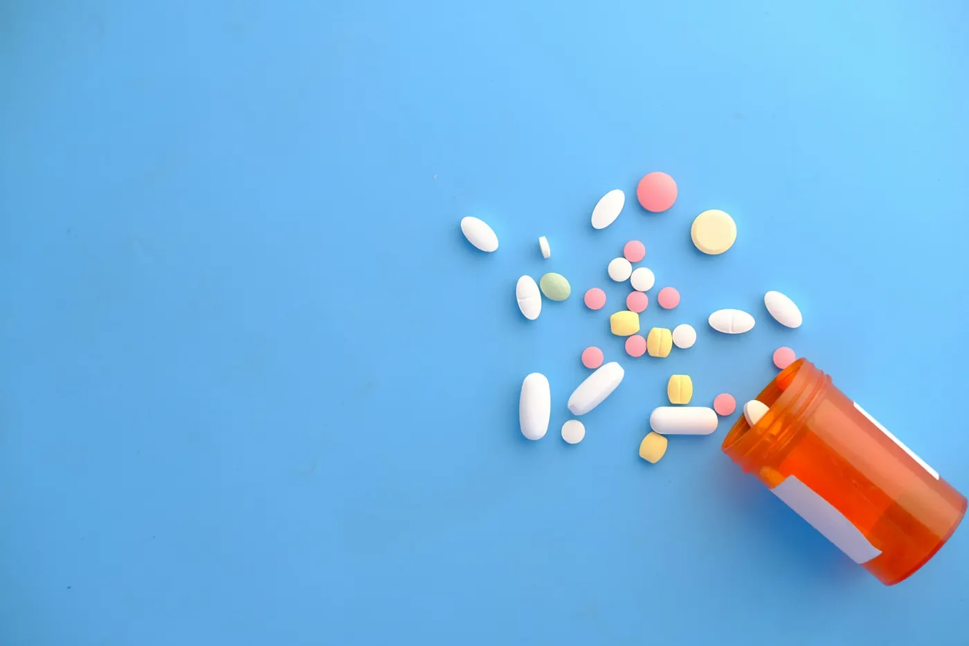Pills spilling from an orange prescription bottle on a blue background